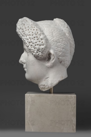 Portrait of a Roman woman, Head with a broad face and an elaborate hairstyle: hair twisted into small curls marked with a gimlet; the rest gathered at the back in a small bun. Round, full face, with a triangular forehead. Female portrait, Roman sculpture, hairstyle, masterpiece. Date: 82–92 CE, place of origin possibly Rome, Roman Empire 27 BC–476. Marble sculpture; height 30.5 cm, width 27 cm, depth 25 cm, weight 36.5 kg., A white marble sculpted head in profile mounted on a rectangular pale beige stone base, shown against a solid dark gray background; the head features textured hair with a perforated curl at the front and a braided or patterned section toward the back, a smooth facial surface with a defined nose, lips, ear, and jawline, and some rougher damaged areas on the lower neck, with small brownish discolorations on parts of the marble.