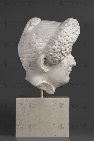 Portrait of a Roman woman, Head with a broad, round full face and a triangular forehead; elaborate hairstyle: hair twisted into small curls marked with a gimlet, the rest gathered at the back in a small bun; female portrait, Roman sculpture, masterpiece; date circa 82–92; origin Rome, — Roman Empire 27 BC–476; sculpture; height 30.5 cm, width 27 cm, depth 25 cm, weight 36.5 kg, A white marble sculpted head shown in profile mounted on a beige marble rectangular base with a short metallic support, the head displaying stylized textured hair with ridged and perforated sections, a visible ear, forehead, nose, lips, and chin, all against a solid dark gray background; colors visible include white, beige, metallic gold, and dark gray.