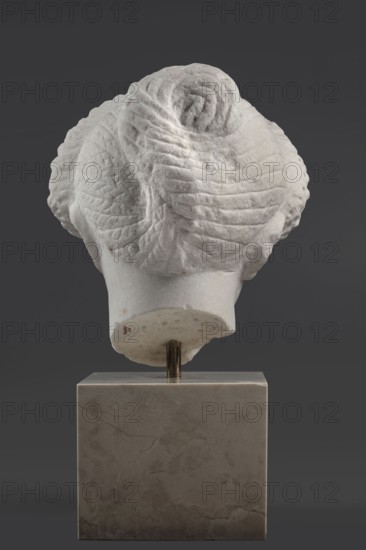Portrait of a Roman woman, Head with a broad face and an elaborate hairstyle: hair twisted into small curls marked with a gimlet; the rest gathered at the back in a small bun. Round, full face, with a triangular forehead. Roman sculpture, female portrait, masterpiece, 82–92 CE, Rome, Roman Empire 27 BC–476, sculpture. Height 30.5 cm, width 27 cm, depth 25 cm, weight 36.5 kg., A rear view of a white stone sculpture of a head with textured, carved hair arranged in tight coils and waves, mounted on a vertical metal rod set into a square gray stone base; the background is dark gray.