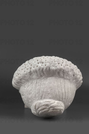 Portrait of a Roman woman, Head with a broad face and an elaborate hairstyle: hair twisted into small curls marked with a gimlet; the rest gathered at the back in a small bun. Round, full face with a triangular forehead. Female portrait, Roman sculpture, hairstyle; Roman Empire 27 BC–476, dated 82–92?; sculpture; height 30.5 cm, width 27 cm, depth 25 cm, weight 36.5 kg., A sculpted object with an off-white, textured surface sits against a dark gray background; the object has a rounded, dome-like top with a series of small, evenly spaced indentations and a ruffled edge, and its lower portion shows vertical grooves and a rolled, layered form at the front, all rendered in the same off-white color with subtle shadows and highlights.