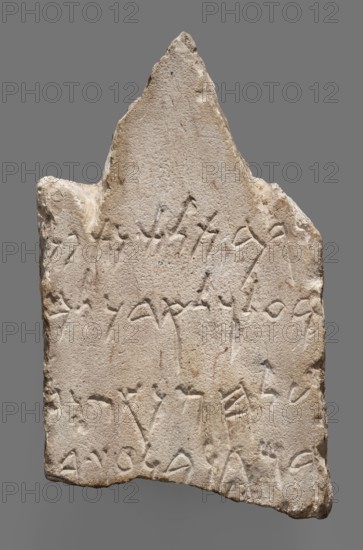 Fragment of a Punic votive inscription, unknown Carthaginian workshop; Baal-Hamon Phoenician deity; Punic stele. Upper part of a stele with acroteria with four lines of inscription: For the Lady, Tanit the Face of Baal, and for the Lord, Baal-Hammon, this is what Magon, son of Azarbaal, offered .... The back side of the object has not been processed and smoothed. 3rd–2nd century BC. Carthage Tunisia. Stele, votive inscription. Height 14.5 cm; width 9 cm; depth 6 cm; weight 1.08 kg., A roughly triangular stone slab with an uneven, chipped edge and a peaked top, showing a textured surface in shades of beige, light tan, and pale cream with small darker brown and gray speckles; the face of the slab bears a few shallow incised marks and grooves arranged in several horizontal groupings, and the sides show irregular breaks and rougher, more eroded areas in similar beige and tan tones against a plain gray background.