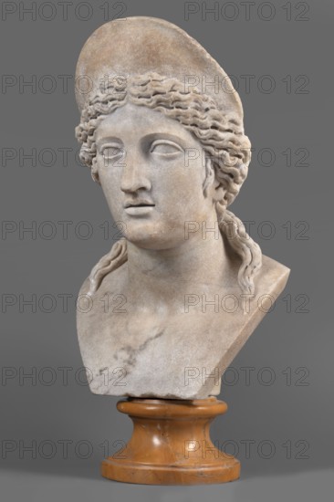 Bust of a woman wearing a diadem, unknown Roman workshop, A woman's head set on a bust, possibly modern. Regular and sharply defined facial features. Strong jaws and chin. Parted lips, straight and long nose with a flat-cut bridge. Almond-shaped eyes under regularly arched eyebrows with sharp edges. Fine waves of hair above the forehead, symmetrically divided into two locks, are pulled back towards the back of the head, obscuring the upper parts of the ears. On either side, at temple level, two small locks of hair fall. The hair is tied in a knot at the back of the head, from under which two locks fall over the shoulders. The head is Juno-type, but there is a strong suspicion that we are dealing with a modern copy. 2nd half 1st century, sculpture, weight 51.5 kg, A carved stone bust of a person with wavy hair and a cap, shown from the shoulders up on a smooth cylindrical orange-brown stone pedestal, with the stone of the bust in pale beige and light gray tones, faint darker gray veinin...