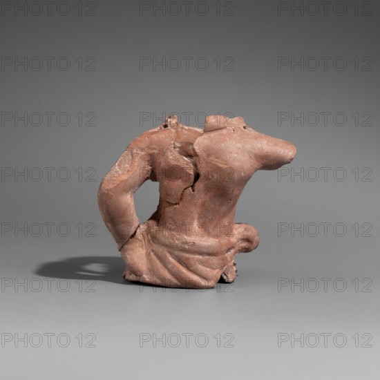 Actor's puppet, Male torso glued together from four fragments. Head, legs, and right arm missing. Around the neck is most likely a torque necklace state of preservation does not allow for precise identification. Left arm bent and resting on hip, torso bare, relatively well-developed, with a clearly marked navel. Body covered from the hips by a garment tied around the right hip. The holes drilled on the hips and arms of the figurine suggest that we are dealing with a fragment of a marionette with movable limbs. 1st century BC. Myrmekion finding site; Pantikapaion regarding the form. Marionette. Height 7.8 cm, width 8.5 cm, depth 4.8 cm., A small weathered terracotta fragment shaped like a torso with an arm, showing a reddish-brown surface with lighter worn patches and rough texture; the piece rests on a smooth gray background that transitions from darker gray at the top to lighter gray at the bottom, and there is a soft shadow beneath the object.