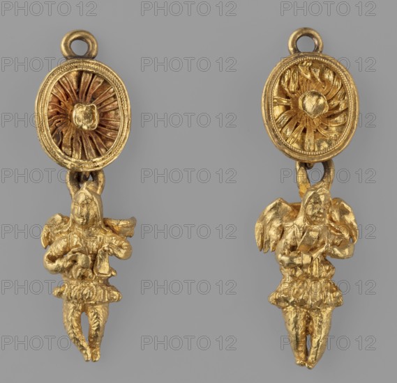 Two earring pendants in the shape of winged Geniuses, Pair of pendants - each composed of 2 parts: 1. Cups - suspended sideways, surrounded by profiled filigree and filled with a rosette with filigree, fastened with a high fitting for a stone missing; the bottom of the cup is reinforced with a soldered strip with a flatly soldered earring at the top and a perpendicularly soldered earring at the bottom. 2. Winged genius, - suspended by the lower earring handle, dressed in a short tunic chiton with hands joined at the front on the chest. The figurines are cast, with soldered wings cut from a single piece of sheet metal each, reinforced with crosswise soldered strips with an eyelet for hanging from a rosette. 1st half of the 3rd century BC, Greece; jewelry; weight 10 g., The image shows a pair of gold-colored dangling ornaments against a gray background, each with an oval top piece featuring a radial, textured central motif and a small loop at the top, connected by a short link to a small...