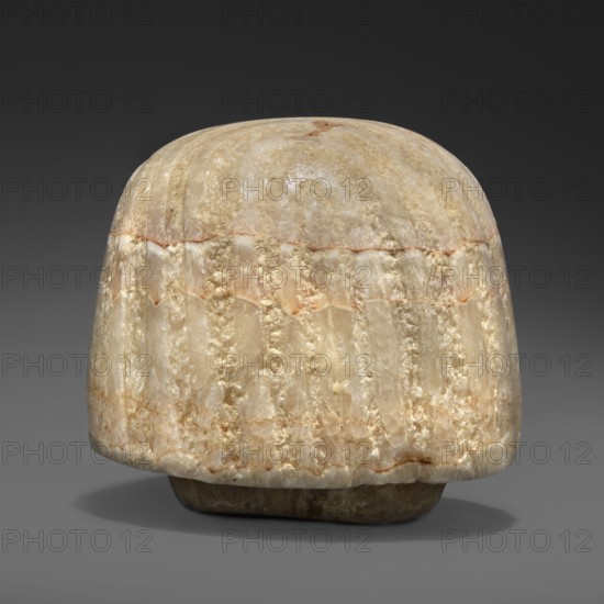 Canopic urn lid in the shape of a human head, Lid of a canopic urn for tomb equipment, associated with the Sons of Horus. Characterized by extremely subtle modelling typical of the Amarna and early post-Amarna periods 2nd half of the 14th century BC: delicate, aristocratic facial features, sfumato around the eyes, and a wig with stripes of varied texture. Dated c. 1350–c. 1295 BC, New Kingdom, end of the 18th Dynasty, Egypt. Materials/measurements: canopic urn lid; height 8.2 cm, width 8.6 cm, depth 9.2 cm, weight 1.124 kg., A roughly dome-shaped carved object sits against a dark gray background, appearing to be made of a translucent stone with a polished surface. The object shows a range of pale colors including beige, cream, off-white, light tan, and hints of warm brown, with subtle banding and veins of slightly darker brownish-orange. The surface texture alternates between smoother, glossy areas and more irregular, crystalline patches that catch the light, and there are vertical flu...