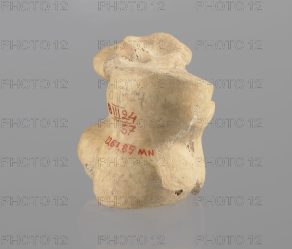 Astragalus of a cow, Myrmekion Crimea, Hellenistic period, astragalus condylo-talus bone of a cow, bones, antiquity, 323–30 BC, found at Myrmekion, product of nature, height 4.6 cm, A beige, irregularly shaped object with a textured, slightly pitted surface sits against a smooth gray background; the object has rounded lobes and depressions with subtle shadows, and its surface shows areas of lighter and darker beige along with small pale white marks and tiny dark spots.