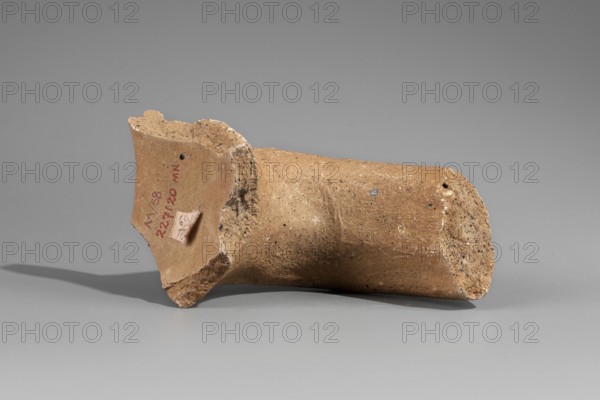 Fragment of the spout and vice of an amphora with a stamp, Papes c. 255–205 BC. Fragment of a Sinopean amphora: preserved spout, neck, and stamped vice. Spout is a semicircular roller; vice is oval in cross-section, flattened. Rectangular four-line stamp; to the right of the legend at height of lines 3–4 an emblem of a grapevine. First line contains the astynomic titulary; second line gives the astynomeus Eucharistos in generic form; third line his patronymic; fourth line the manufacturer name Papes in generic form. Attributed to M. Matera; 2nd half of 3rd century BC. Findspot: Myrmekion; origin: Sinope. Attributes: Sinopean stamp, vice; height 9.2 cm., A broken cylindrical clay fragment lying on its side on a smooth surface, with rough, uneven edges and a flared rim at one end; the fragment is predominantly brown and tan with speckles of darker brown and small lighter flecks, and it casts a soft shadow on the gray background.