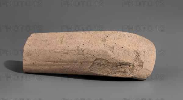 Fragment of a stamped amphora vice, Agathon II ca. 250–205 BC. Fragment of a Sinopean amphora vice with a partially preserved rectangular stamp. The stamp is oval in cross-section, flattened, located on the bend of the vice. Originally a four-line stamp: the first line of the legend is not impressed; the last line is partially preserved only upper parts of letters visible; the last two letters missing. To the right of the legend was an emblem in the form of a prora. Originally the first line contained the astynomic title; the second line contained the name of the astynomeus Delphios, expressed in the generic form; the third line is his patronymic; the fourth line contains the name of the manufacturer Agathon II, in the nominative. 2nd half of the 3rd century BC. Findspot: Myrmekion Crimea. Origin: Sinope. Stamp; vice; height 12.8 cm., A single elongated object with a rough, granular surface rests on a flat background; the object is primarily beige with darker speckles and patches of sl...