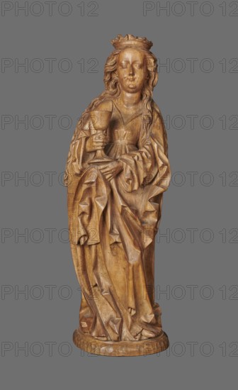 Figure of St. Barbara, sculptor unknown. Medieval wall sculpture, hollowed out from behind the head also has a circular hollow. Depicts St. Barbara in contrapposto, creating an S-shaped silhouette. Slightly oversized head on a cylindrical neck; elongated face with high forehead, straight narrow nose, full cheeks; small smiling mouth creating dimples in cheeks and a dimple in the chin. Long hair framed in thin parallel wavy strands, falling down her back with a strand over her right shoulder. Wears a crown finial broken. Right hand grasps the stem of a chalice attribute of St. Barbara; left hand, fingers covered by cloak, supports the chalice from beneath. Dress with triangular neckline and long wide sleeves, cinched at the waist with a decorative belt; voluminous cloak with numerous folds and dry thin ridges. Pointed left shoe peeks from beneath folds. Base round and irregularly carved. No polychrome. Circa 1500, possibly Silesia. Sculpture; height 102.0 cm, width 35.0 cm, depth 24.0 c...