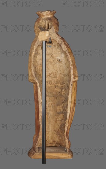 Figure of St. Barbara, St. Barbara d. 306. Medieval wall sculpture, hollowed out from behind the head also has a circular hollow. Depicts St. Barbara in contrapposto, creating a slight S-shaped silhouette. Slightly oversized head on a cylindrical neck; elongated face with high forehead, straight narrow nose, full cheeks, small smiling mouth with dimples and a dimple in the chin. Long hair framing the face and falling down the back, one strand draped over the right shoulder, carved as thin parallel wavy strands. Wears a crown finial broken. Right hand grasps the stem of a chalice, left hand fingers covered by a cloak supports the foot of the chalice. Dress with triangular neckline and long wide sleeves, cinched at the waist with a decorative belt; voluminous cloak with numerous folds formed into dry, thin ridges. Pointed left shoe peeking from beneath folds. Round, irregularly carved base. No polychrome. Ca. 1500, probably Silesia. Sculpture. Height 102.0 cm; width 35.0 cm; depth 24.0 c...