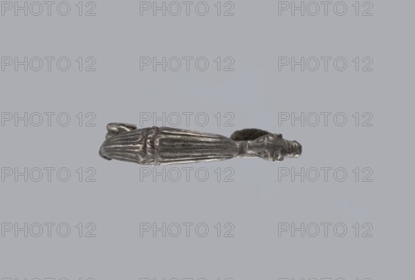 Snake-headed fibula, unknown Southern Italian workshop. Fibula with an arched, thick hoop. The hoop is terminated on one side with an imitation spiral, and on the other side connected to the rectangular wall of the sheath, bent at the bottom. A cylindrical leg extends from the sheath, bent towards the hoop, ending with a snake's head. The hoop is decorated with numerous longitudinally engraved lines. Condition: corrosion, missing needle. 5th–4th century BC, Southern Italy. Materials: silver. Iconography: snake., A metallic object with a silver-gray finish is shown against a pale gray background; it appears elongated with a tapered central section featuring raised ridges and fluting, a rounded end with a small protrusion, and a ring-like opening at the opposite end that has an irregular, textured surface; the metal shows darker gray shadows and lighter silver highlights across its surface.