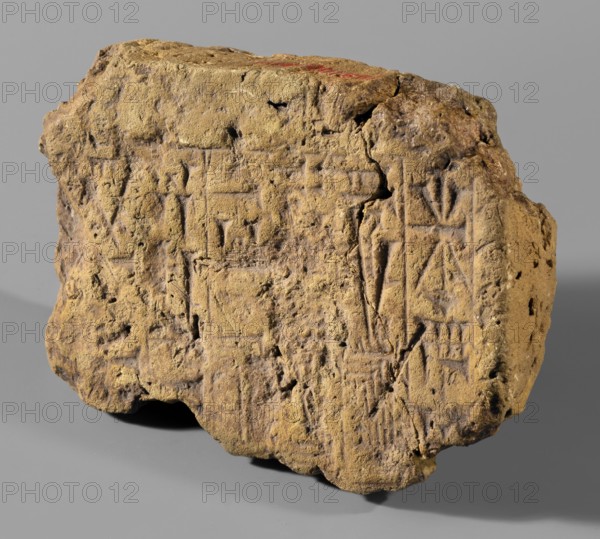 Fragment of a brick with a cuneiform inscription, impressed with a stamp; fragment with 6 lines of archaized cuneiform recording an inscription of Neo-Babylonian king Nebuchadnezzar II Nabu-kudurri-usur, reign 604–562 BC. Associated names/places in the inscription: Esagila temple of Marduk, Babylon and Ezida temple circle, Babylon. Neo-Babylonian period, 604–562 BC. Possibly from Babylon or Borsippa. Material: brick; weight 344 g; width 11.8 cm; height 8.6 cm; thickness 3.2 cm., A rough, irregularly shaped block of hardened material with a coarse, pitted surface, shown against a plain neutral background; the block displays a predominantly sandy yellowish-brown color with areas of darker brown and small patches of reddish tint on the upper surface, and its surface bears shallow incised marks and linear grooves forming geometric patterns; the edges are uneven and chipped, and the underside casts a soft shadow on the background.
