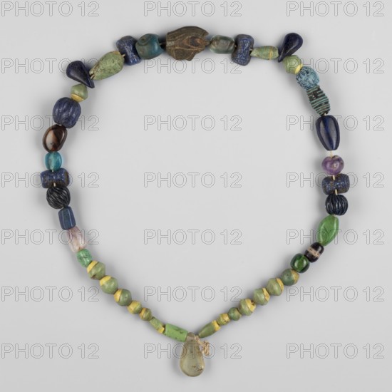 Necklace of 43 different beads, Goluchów Greater Poland Voivodeship. Scaraboids, udjat eyes, ornaments. Necklace consisting of 43 beads, including an udjat eye and 4 glass beads depicting a bearded face. Among the others, biconical and cylindrical beads made of green glass combined with yellow predominate, but many other shapes and colors can be found here - teardrops of black obsidian, an amethyst ball, melon-shaped beads made of dark glass, a quartz flower petal and many others. 664 BC – 395, Egypt; jewelry, amulet; length 38 cm., A necklace composed of a group of beads arranged in a loop, featuring a teardrop-shaped pendant at the bottom tied with a small cord; the beads show a variety of shapes including rounded, elongated, faceted, and ribbed forms. The visible colors include shades of green, blue, yellow, purple, black, brown, turquoise, and teal, with some beads showing mixed or mottled tones. Several beads have a smooth glossy surface, a few have matte or weathered textures, an...