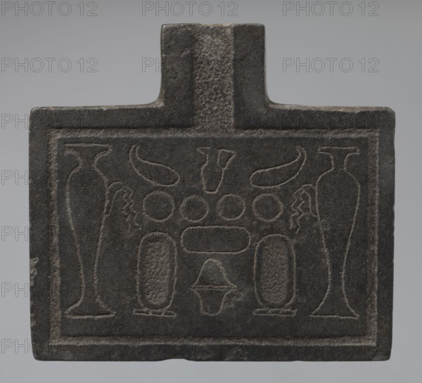 Nesichnum's sacrificial table, sacrificial formulas, vases, breads, cartouches, Nesichnum ca. 332–330 BC, ritual vessels iconographic, hieroglyphs; Ptolemaic Period, Egypt, sacrificial table; height 5.5 cm, width 23 cm, depth 23 cm, A rectangular dark gray stone plaque with a raised rectangular border and a short protruding tab at the top, featuring shallow carved motifs including paired tall vase-like shapes near the sides, a group of rounded shapes and elongated ovals in the central area, two curved horn-like forms near the top center, and a small triangular form near the lower center; the stone surface shows textured and smoother areas in shades of dark gray and black against a light gray background.