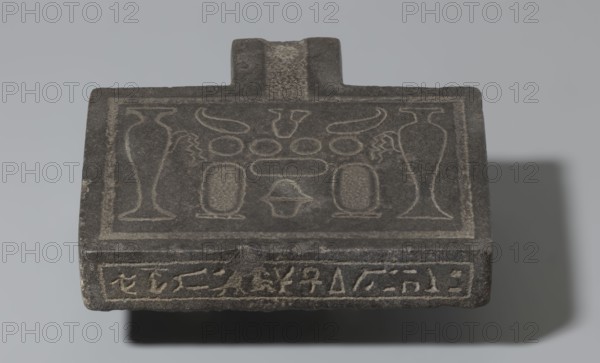 Nesichnum's sacrificial table; sacrificial formulas, vases, breads, cartouches, Nesichnum ca. 332–330 BC; ritual vessels iconographic; hieroglyphs; Ptolemaic Period, Egypt 332–30 BC; sacrificial table; height 5.5 cm, width 23 cm, depth 23 cm., A flat, rectangular stone object with a raised handle-like protrusion at one edge, showing carved linear designs and shallow relief motifs across its top surface; the stone appears predominantly dark gray with lighter gray incised lines highlighting the decorative patterns, and a shadow cast behind and below the object in darker gray tones.