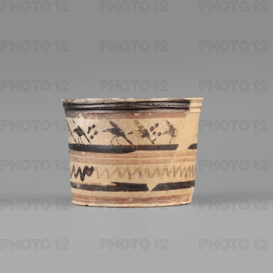 Pyxis with a duck motif. Greek, Boeotian, early 7th century BC. Clay yellowish/light gray to very pale brown with brown varnish and dark brown matte paint; red paint light reddish brown. Vessel with flat bottom, walls slightly flaring toward a profiled rim. Banded decoration: upper band shows a row of birds walking to the right in silhouette with lowered heads and raised wings; dotted rosettes between pairs of birds. Below, decoration enclosed in two wide dark bands consisting of two watered-firnis stripes and a zigzag line. Dimensions: depth 5.5 cm; diameter 7.3 cm; wall thickness 0.4 cm; height 6.5 cm; width 8.8 cm; weight 0.098 kg., A short cylindrical ceramic vessel sits against a plain gray background, showing a beige to light tan base color with decorative bands in darker brown and black. The rim is slightly flared and darker, with visible wear and chipping revealing lighter beige beneath. Around the upper part of the vessel are dark painted motifs including abstract birdlike sha...