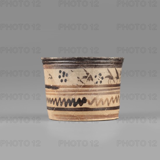 Pyxis with a duck motif. Vessel of yellowish clay covered with dark brown matte varnish; upper band shows a row of birds ducks striding right in silhouette with lowered heads and raised wings, pairs separated by dotted rosettes. Below the birds, decoration enclosed by two wide dark bands consisting of two stripes of watered varnish and a zigzag line. Profiled rim, flat bottom, walls slightly flaring toward the rim. Banded decoration; painted with black varnish and light reddish-brown paint. Early 7th century BC attributed. Boeotia. Pyxis container. Dimensions: depth 5.5 cm; diameter 7.3 cm; wall thickness 0.4 cm; height 6.5 cm; width 8.8 cm; weight 0.098 kg. Clay colour: 10 YR 7/2–10 YR 7/4; varnish colour: 2.5 YR 2.5/1; red paint: 2.5 YR 6/3., A cylindrical ceramic vessel with a slightly flared rim sits against a neutral background. The vessel shows a base color of beige or light tan with painted decorative bands in dark brown and black. Near the top there is a darker brown rim follow...