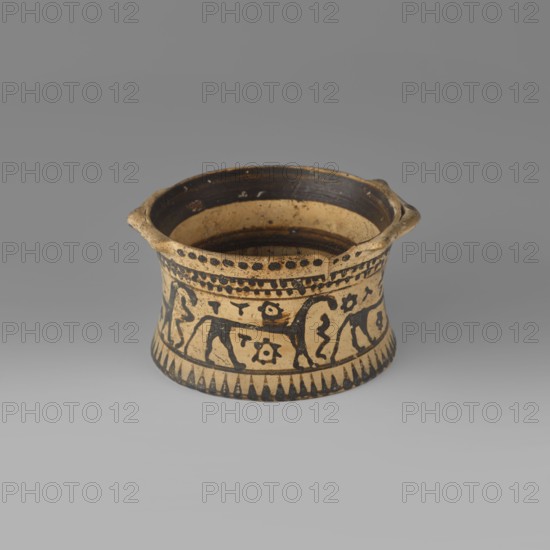 Orientalising pyxis with an animal frieze in the Silhouette style, Images of animals, Middle Corinthian period, cats. Thin-walled pyxis with a straight rim, slightly concave body walls, and a flat bottom. Small vices mounted horizontally just near the edge of the rim. The main decorative band, bounded at the top and bottom by a thin line of varnish, depicts figures of animals executed using the silhouette technique. Between the silhouettes there are simplified filling ornaments. Clay color: 5 Y 8/2 pale yellow Varnish color: 5 Y 2.5/1 black 590–570 BC dated to the Middle Corinthian period, Corinth. Pyxis, vessel; height 5.3 cm, width 10.2 cm, depth 8.5 cm, weight 0.102 kg., A small shallow ceramic vessel sits on a neutral gray surface against a gray background, showing a beige base color with dark brown to black painted decoration; the vessel flares outward slightly toward the top and has a short foot at the bottom, with two small protruding handles near the rim; the interior is dark b...