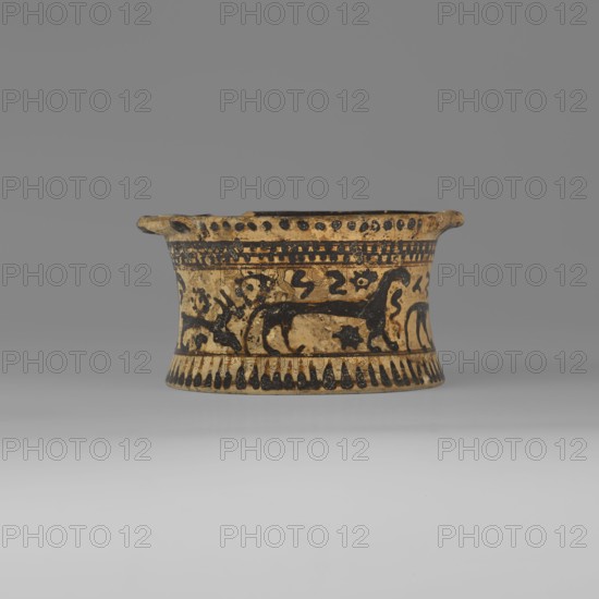 Orientalising pyxis with an animal frieze in the Silhouette style, images of animals, Middle Corinthian period, cats. Thin-walled pyxis with a straight rim, slightly concave body walls, and a flat bottom. Small vices mounted horizontally just near the edge of the rim. The main decorative band, bounded at the top and bottom by a thin line of varnish, depicts figures of animals executed using the silhouette technique. Between the silhouettes there are simplified filling ornaments. Clay color: 5 Y 8/2 pale yellow Varnish color: 5 Y 2.5/1 black 590–570 BC Middle Corinthian period, Corinth, pyxis vessel, height 5.3 cm, width 10.2 cm, depth 8.5 cm, weight 0.102 kg, A shallow, round ceramic vessel in beige and black sits centered against a neutral gray background, with a flared rim and a slightly concave body. The surface shows painted black decorative bands and motifs, including stylized animal silhouettes and abstract shapes encircling the midsection, a band of alternating dash-like marks a...