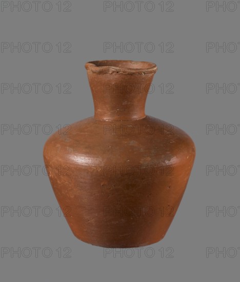 Jug, ceramics, Egyptian pottery. Medium-sized clay jug with a biconical body, widest at about half its height; wide shoulders; wide, almost cylindrical neck widening toward the spout neck about one-third of total height. Profiled, irregular spout, slightly raised and extended on one side forming a small spout; spout nearly triangular in cross-section with a ~1 mm cylindrical bulge on the outer profile. Bottom almost flat, very slightly rounded. Made of Nile clay NB1?; neck likely made separately and attached to the shoulders. Outer surface leveled, covered with engobe and polished; inner surface leveled except for neck, which is also engobed and polished. Color reddish-brown. Well preserved; rim slightly chipped in two places and engobe worn in places on outer surface. Dated to the 6th Dynasty; origin Edfu. Dimensions of a comparable type: height 20.5 cm, rim diameter 8.5 cm, body diameter 17.3 cm, bottom diameter 10.9 cm. Analogous example in the Louvre E 16586. References: Reisner, M...