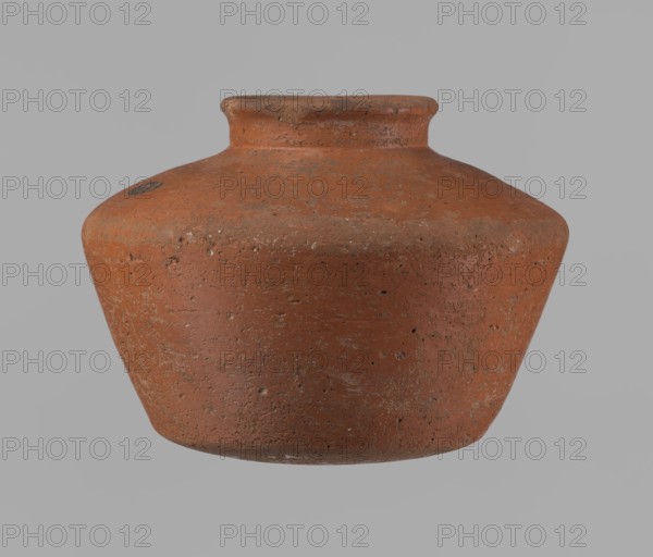Vessel, unknown creator; Egyptian pottery vessel clay, c. 2686–c. 2181 BC Old Kingdom, from Edfu; height 11 cm, rim diameter 6.3 cm, body diameter 14.7 cm, bottom diameter 10 cm., A rounded, squat clay vessel with a short neck and flared rim sits against a plain background; the vessel's surface is textured with small pits and rough patches and shows variations of reddish-brown and terracotta tones with areas of darker brown and traces of lighter, almost grayish wear.