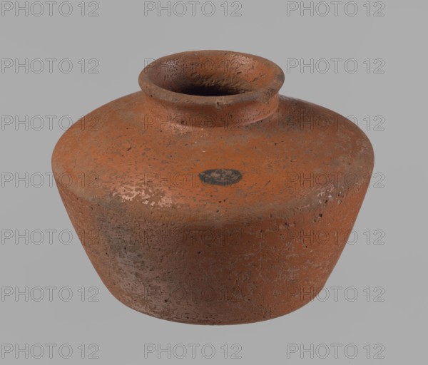 Vessel, Egyptian pottery vessel made of clay, c. 2686–c. 2181 BC Old Kingdom, from Edfu. Height 11 cm; rim diameter 6.3 cm; body diameter 14.7 cm; bottom diameter 10 cm., A rounded earthenware vessel with a wide body and a short, narrow neck, showing a rough, pitted surface texture and worn areas; the vessel appears primarily reddish-brown with patches of darker brown and small areas of lighter, pale spots, set against a plain light gray background.
