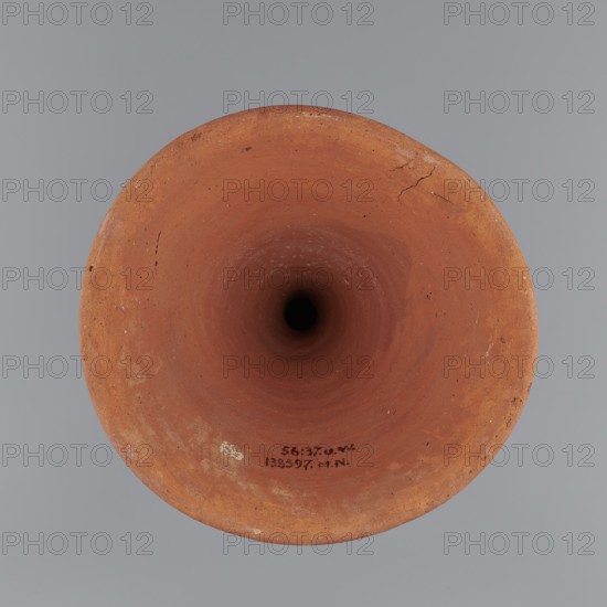 Bowl base. Base for a vessel with an almost equal diameter of both rims; both rims irregular with a wavy line. Center of the base is empty. The narrowest part of the base is approximately 2/3 of the height of the entire vessel. Made of Nile clay NB1. Surface leveled, covered with an engobe, then polished. Vessel color: red. Complete, very well preserved. c. 2494–c. 2181 BC; Old Kingdom, 5th–6th Dynasty, Edfu find place. Vessel; diameter top 17.5 cm, diameter bottom 18 cm, height 25.6 cm, weight 1.30 kg., A top-down view of a round terracotta object with an open circular mouth leading to a dark central hole, showing a rough, slightly uneven rim with small cracks and surface imperfections; the visible colors include shades of reddish-brown, orange, and darker brown within the interior, contrasted against a smooth gray background.