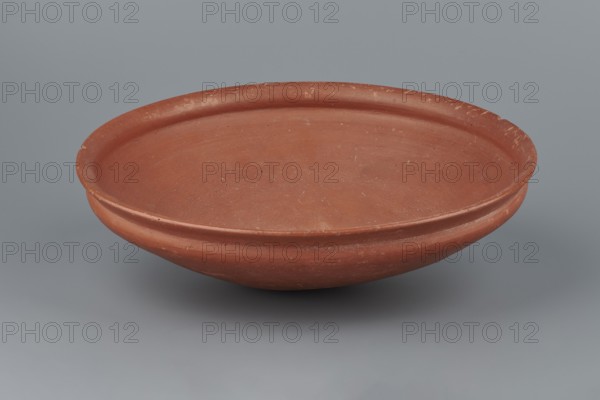 Medum-type bowl, Egyptian pottery, Medum-type bowl. Clay vessel with hemispherical shape narrowing just below the rim to form a carination; rounded bottom and straight, slightly widening spout whose diameter is slightly larger than the shoulders. Surface even, covered with a red engobe and polished. Vessel color: red. Fairly well preserved with minor losses on the rim. c. 2494–c. 2181 BC; Old Kingdom, 5th–6th Dynasty, Edfu. Vessel, height 7 cm, diameter 26.4 cm spout, weight 0.90 kg., A shallow, round terracotta bowl with a slightly raised rim sits against a smooth gray background; the bowl shows a reddish-brown color with lighter and darker variations, a few small speckles and scuffs, and a subtle horizontal ridge around its exterior.