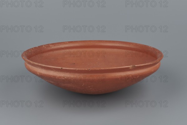 Medum-type bowl, Egyptian pottery, Medum-type bowls. Clay vessel with hemispherical shape narrowing just below the rim to form a carination; rounded bottom; straight, slightly widening spout whose diameter is slightly larger than the shoulders. Surface even, covered with red engobe and polished. Vessel color: red. Fairly well preserved with minor losses on the rim. c. 2494–c. 2181 BC; Old Kingdom, 5th–6th Dynasty, Edfu. Vessel; height 7 cm; diameter 26.4 cm spout; weight 0.90 kg., A shallow round dish with a raised rim in terracotta red, showing a smooth matte surface with areas of lighter wear and small dark spots, set against a cool gray background.