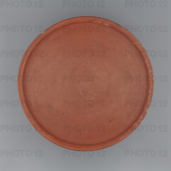 Medum-type bowl, Clay vessel with hemispherical shape narrowing just below the rim to form a carination; rounded bottom; straight, slightly widening spout whose diameter is slightly larger than the shoulders. Surface even, covered with red engobe and polished. Vessel color: red. Fairly well preserved with minor losses on the rim. Circa 2494–2181 BC, Old Kingdom, 5th–6th Dynasty, Edfu. Vessel; height 7 cm, spout diameter 26.4 cm, weight 0.90 kg., A round shallow dish with a raised rim shown from above, predominantly terracotta in color with a few small darker specks and tiny lighter flecks on its interior surface, set against a smooth gray background.