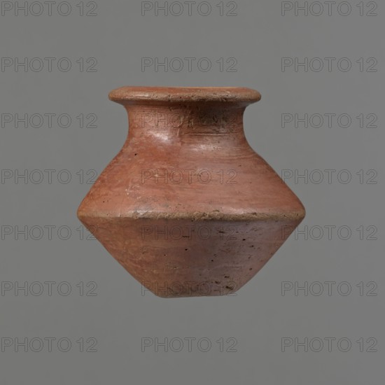 Vessel, Egyptian pottery ceramic clay vessel, c. 1650–c. 1550 BC Second Intermediate Period, found at Edfu; vessel, height 7.4 cm, diameter 5.5 cm rim, diameter 8.2 cm belly, A single terracotta vessel with a rounded body that tapers to a point at the bottom and a short flared neck at the top is centered against a plain gray background; the vessel shows a textured surface with small pits and irregularities and displays shades of reddish-brown and muted orange with areas of darker brown and subtle lighter patches.