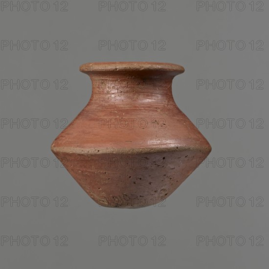 Vessel, Egyptian pottery ceramic clay vessel, c. 1650–c. 1550 BC Second Intermediate Period, findspot Edfu; vessel height 7.4 cm, rim diameter 5.5 cm, belly diameter 8.2 cm., A clay pot suspended against a plain gray background, showing a rounded body that tapers to a narrow base and flares outward to a short neck with a wide, flat rim; the pot has a weathered, rough surface with small pits and irregularities and displays shades of reddish-brown and muted tan with subtle variations in tone and slight darker speckling.