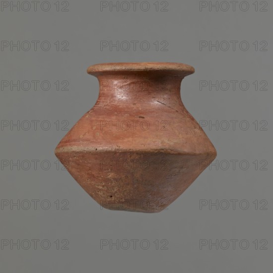 Vessel, Egyptian pottery ceramic clay vessel, c. 1650–c. 1550 BC Second Intermediate Period, from Edfu; vessel height 7.4 cm, rim diameter 5.5 cm, belly diameter 8.2 cm., A single clay vessel with a wide, flared rim and a tapered, angular body is centered against a plain gray background; the surface of the vessel shows a weathered, rough texture with small pits and irregularities and its colors include reddish-brown, terracotta, muted orange, and a few darker brown patches.
