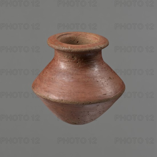 Vessel, Egyptian pottery ceramic clay vessel, c. 1650–c. 1550 BC Second Intermediate Period, Edfu, vessel, height 7.4 cm, rim diameter 5.5 cm, belly diameter 8.2 cm., A single rounded clay vessel with a wide flared rim and a bulbous body is shown against a plain background; the surface of the vessel is textured with small pits and irregularities and shows wear and slight chipping along the rim and edges, and the visible colors include terracotta red, muted brown, and small areas of darker brown.