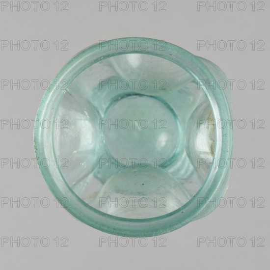 Glass cup, Egypt, 1st–2nd century AD. Type: Isings form 32. Transparent bluish-green glass. Cup with a slightly flaring spout, decorated with four oval concavities on the belly. Ring-shaped foot with a clearance made by pressing the bottom inward; free-blown. Outer diameter of the spout: 6.10 cm. Height: 9 cm. Belly diameter: 6.70 cm. Outer diameter of the bottom: 4.60 cm. Vessel, weight 0.054 kg., A close-up top view of a translucent glass container in a pale aqua color against a light gray background, showing the rounded rim and the bulbous interior surfaces with a few small bubbles and subtle iridescent reflections, and areas of slightly lighter and darker aqua tones on the curved glass.