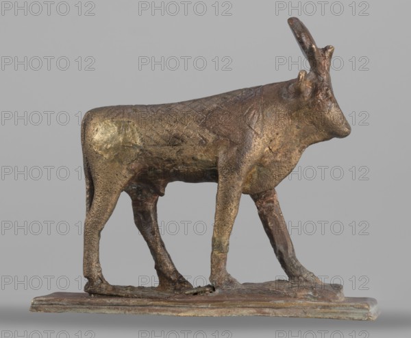 Apis bull figurine, Apis mythology, bulls, Scen.Gal.Eg., sacred animals, animal figurines, Egyptian art, Sacred animal of the god Ptah, 664–525 BC; Late Period, 26th Dynasty, Egypt, figurine, height 7 cm, width 6 cm, weight 0.164 kg, A small bronze-colored sculpture of an animal with a textured body and elongated head stands on a rectangular base; the figure shows a metallic sheen with areas of golden, brown, and greenish patina, a pair of upward-pointing horns, a slightly rough surface with subtle tool marks, slender legs positioned as if walking, and the base appears weathered with similar bronze and green tones against a neutral gray background.