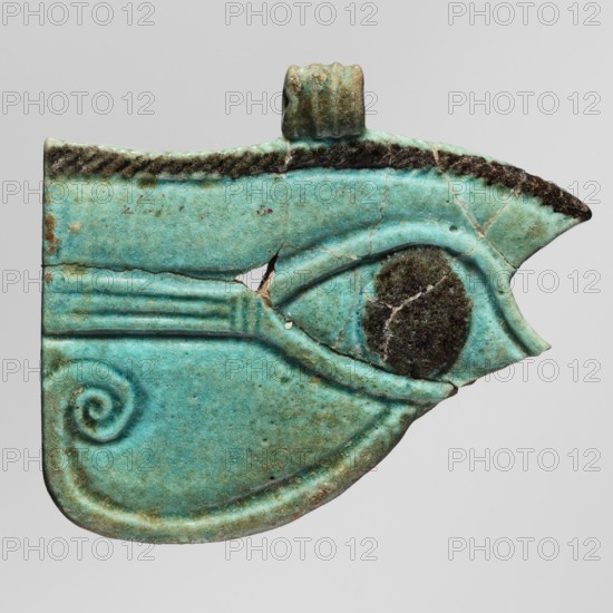 Amulet - udjat eye;, protective amulet/pendant, grave good; ca. 747–656 BC, Third Intermediate Period, 25th Dynasty, Egypt; material not specified; height 4.7 cm, width 5.6 cm, A flat, turquoise-green object shaped like a stylized eye with a pointed outer tip and a rounded inner curve, showing a darker, nearly black circular area at the center of the eye. The surface has visible cracks and a small missing chip near the middle, plus a rough, darker brown edge along the top and at the pointed tip. There is a small raised loop or loop-like projection at the top, and a raised spiral motif near the lower left within the curved area. The colors visible include turquoise, green, brown, dark brown, and a little pale tan.