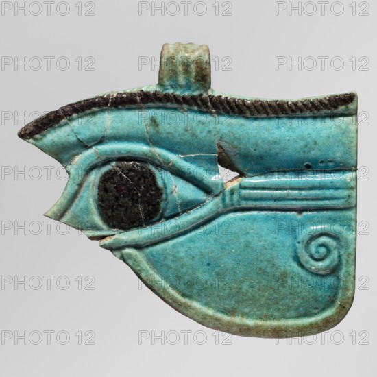 Amulet - udjat eye;, protective amulet/pendant and grave good; udjat eyes; ca. 747–656 BC, Third Intermediate Period, 25th Dynasty, Egypt; height 4.7 cm, width 5.6 cm, A glazed turquoise-blue object shaped like a stylized eye with a raised rim and carved linear details, showing a dark circular inlay at the center of the eye and a textured dark ridge along the top edge; the surface has a few visible cracks and small chips revealing a pale material beneath, and there is a spiraled raised motif near the lower right.