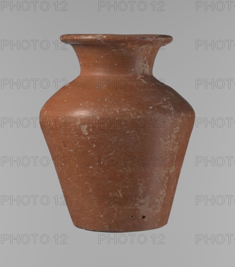Vessel, Egyptian pottery ceramic clay vessel, conical, widest at approximately 3/4 of its height. Shoulders wide, almost horizontal, slightly sloping. Neck wide, short, funnel-shaped, widening towards the spout. Spout wide, flat in the upper part, slightly rounded at the bottom, slightly asymmetrical. Bottom slightly convex, asymmetrical. Surface even. Lower part worked to approximately 2/3 of its height with a knife or similar tool. Outer surface and inner surface of rim and neck covered with a layer of dark red engobe. Color dark red. Vessel complete; surface eroded in many places, numerous clay chips on the rim. Old Kingdom, ca. 2686–2181 BC; provenance: Edfu. Height 16.7 cm; rim diameter 9.5 cm; body diameter 13 cm; bottom diameter 8.1 cm. References: Reisner, Mycerinus, p. 219, types XIX and XX, fig. 69., A single terracotta-colored ceramic vessel with a rounded shoulder, flared rim, and tapered base, showing areas of worn and chipped surface with lighter beige and off-white patch...