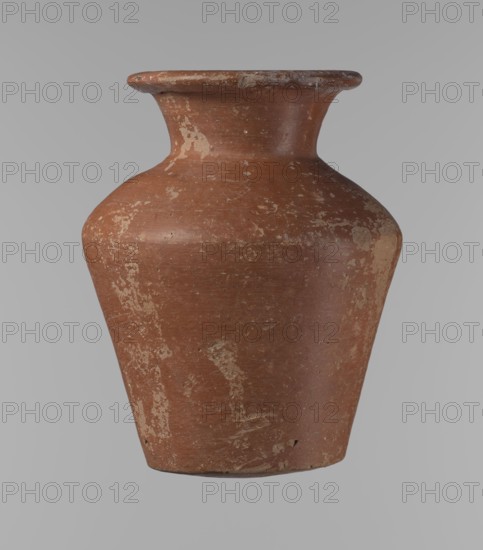 Vessel, Egyptian pottery, ceramic clay vessel; a conical vessel, widest at approximately 3/4 of its height. The shoulders are quite wide, almost horizontal—slightly sloping. The neck is wide, short, funnel-shaped, widening towards the spout. The spout is wide, flat in the upper part, slightly rounded at the bottom, slightly asymmetrical. The bottom is slightly convex, asymmetrical. The surface of the vessel is even. The lower part has been worked to approximately 2/3 of its height with a knife or similar tool. The outer surface and the inner surface of the rim and neck are covered with a layer of dark red engobe. Vessel color: dark red. Vessel complete; surface eroded in many places, numerous clay chips on the rim. ca. 2686–2181 BC, Old Kingdom, Edfu; height 16.7 cm, rim diameter 9.5 cm, body diameter 13 cm, bottom diameter 8.1 cm., A single ceramic vase with a wide flared rim, a narrow neck, a rounded shoulder, and a tapered body is shown against a plain background; the vase is primar...
