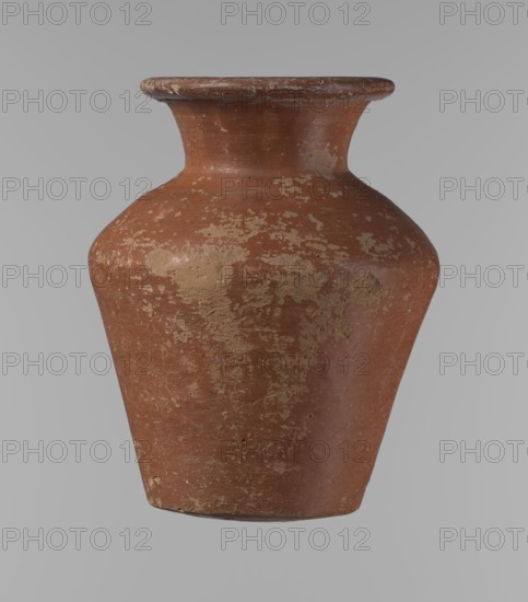 Vessel, Egyptian pottery, clay vessel; conical shape, widest at approximately 3/4 of its height. Shoulders wide and almost horizontal, slightly sloping. Neck wide, short, funnel-shaped, widening toward the spout. Spout wide, flat in the upper part, slightly rounded at the bottom, slightly asymmetrical. Bottom slightly convex, asymmetrical. Surface even. Lower part worked to approximately 2/3 of its height with a knife or similar tool. Outer surface and inner surface of rim and neck covered with a layer of dark red engobe. Vessel color dark red. Vessel complete; surface eroded in many places with numerous clay chips on the rim. Attributed to ca. 2686–2181 BC, Old Kingdom, Edfu. Height 16.7 cm; rim diameter 9.5 cm; body diameter 13 cm; bottom diameter 8.1 cm. References: Reisner, Mycerinus, p. 219, types XIX and XX, fig. 69., A single aged ceramic vase with a wide flared rim and a rounded shoulder tapering to a narrower base is shown against a plain neutral background. The surface of the...