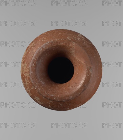Vessel, Egyptian pottery, ceramic clay vessel. A conical vessel, widest at approximately 3/4 of its height. The shoulders are wide, almost horizontal to slightly sloping. The neck is wide, short, funnel-shaped, widening towards the spout. The spout is wide, flat in the upper part, slightly rounded at the bottom, slightly asymmetrical. The bottom is slightly convex, asymmetrical. The surface is even. The lower part of the vessel has been worked to approximately 2/3 of its height with a knife or similar tool. The outer surface and the inner surface of the rim and neck are covered with a layer of dark red engobe. Vessel color: dark red. Vessel complete; surface eroded in many places, with numerous clay chips on the rim. Old Kingdom, ca. 2686–2181 BC; Edfu. Height 16.7 cm; diameter 9.5 cm rim, 13 cm body, 8.1 cm bottom., A top-down view of a round, terracotta-colored clay vessel with a wide rim and a deep, dark interior, showing areas of lighter discoloration and surface wear on the reddis...
