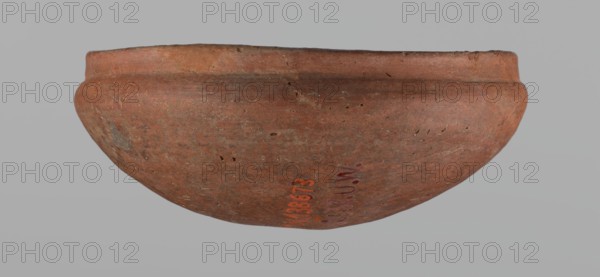 Medum-type bowl, A small Medum-type bowl with characteristic carination under the rim. Rounded bottom. Arched walls, gently breaking towards the center of the vessel around 2/3 of its height. Straight, perpendicular rim. Narrow, sloping shoulders. The diameter of the rim is significantly smaller than the diameter of the vessel's arms. Clay probably NB2. Surface leveled and covered with a layer of engobe, then polished. Vessel color: red. c. 2686–c. 2181 BC; Old Kingdom, Edfu. Vessel; height 4.5 cm, diameter 11 cm rim, diameter 11.6 cm arms., A rounded clay bowl shown from the side with a curved rim and a gently bulging body, displaying a textured surface with small pits and scratches; the bowl is primarily reddish-brown with variations of darker brown and subtle grayish patches, and the background is a uniform light gray.