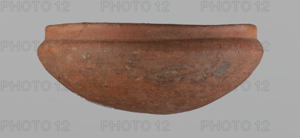 Medum-type bowl, small Medum-type bowl with characteristic carination under the rim. Rounded bottom. Arched walls, gently breaking towards the center of the vessel around 2/3 of its height. Straight, perpendicular rim. Narrow, sloping shoulders. The diameter of the rim is significantly smaller than the diameter of the vessel's arms. Clay probably NB2. Surface leveled and covered with a layer of engobe, then polished. Vessel color: red. c. 2686–c. 2181 BC; Old Kingdom, Edfu. Vessel; height 4.5 cm, diameter 11 cm rim, diameter 11.6 cm arms., A rounded, shallow ceramic bowl occupies the center of the image against a plain light gray background; the bowl is primarily reddish-brown with patches of darker brown and muted orange, and it shows a weathered, slightly rough surface texture with small pits and irregular marks, a rounded lip with a subtle ridge near the rim, and some areas of lighter beige and grayish discoloration scattered across the exterior.