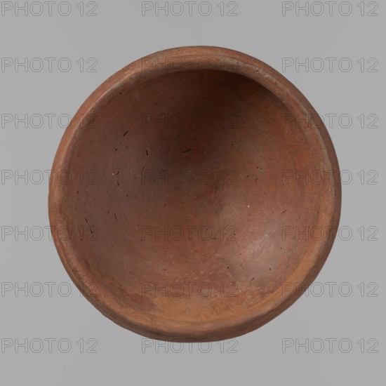 Medum-type bowl, A small Medum-type bowl with characteristic carination under the rim. Rounded bottom. Arched walls, gently breaking towards the center of the vessel around 2/3 of its height. Straight, perpendicular rim. Narrow, sloping shoulders. The diameter of the rim is significantly smaller than the diameter of the vessel's arms. Clay probably NB2. The vessel's surface is leveled and covered with a layer of engobe, and then polished. Vessel color - red. c. 2686–2181 BC; Old Kingdom, Edfu. Vessel; height 4.5 cm, diameter 11 cm rim, diameter 11.6 cm arms., A top-down view of a round, shallow bowl with a smooth continuous rim, showing an interior surface with a worn, slightly uneven texture and tiny pits and scratches. The bowl is primarily reddish-brown with areas of darker and lighter brown, and subtle hints of ochre and grayish tones along the rim and inner curve. The background is a flat neutral gray.