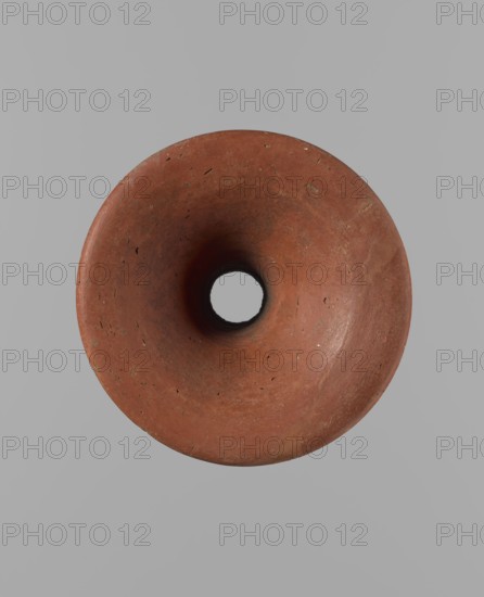 Bowl stand, unknown creator. Base for a vessel with an almost equal diameter of both rims. Both rims are irregular, with a slightly wavy line. The center of the base is empty. The narrowest part of the base is approximately 2/3 of the height of the entire vessel. Made of Nile clay NB2. Surface leveled, covered with an engobe, then polished. Vessel color: red. Complete, very well preserved. Set with bowl. Ca. 2494–ca. 2181 BC; Old Kingdom, 5th–6th Dynasty, Edfu. Vessel; height 13.7 cm; diameter 10.2 cm rim; diameter 9.3 cm bottom., A top-down view of a round, hollow object with a smooth, concave interior and a central circular opening, showing a worn terracotta surface with small pits and irregularities in shades of reddish-brown and darker brown, set against a plain light gray background.