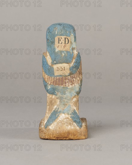 Figurine of the Soul of Ba, Ba mythology; birds; bird iconography; djed pillars; wigs; Soul personification; figurine with beards and feathers. The figurine has carefully carved and painted facial details and a reproduced arrangement of feathers on the wings. On the head is a tripartite wig painted blue. On the chest below the wig is a depiction of a djed pillar. Straps supporting a false beard are painted along the cheeks. The figurine's disproportionately large feet rest on a rectangular base. Late Period, Egypt, 664–332 BC. Object: figurine; height 11 cm, width 9.5 cm, depth 4.5 cm., A small carved wooden figure shown from the back, painted mainly in blue with areas of worn beige and brown where the paint has chipped; the figure sits on a rectangular base that is natural wood brown and weathered, and there is a pattern of blue paint extending down the back and onto the base, with traces of darker brown and lighter off-white showing through.