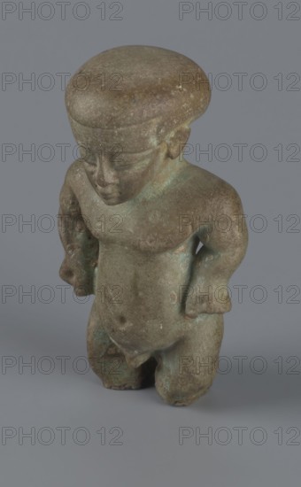 Amulet - Ptah-dwarf Pataikos, Ptah-dwarf mythology. Figurine of a naked dwarf man with a large head with a wide forehead, short arms with clenched fists pressed to the hips, and short legs broken off at the knees. Careful modelling. 7th–4th century BC, Late Period, Egypt. Figurine/amulet. Dimensions: height 6.5 cm; width 3.7 cm; depth 2.6 cm., A small sculpted figure rendered in mottled brown and greenish tones stands against a plain gray background, showing a rounded head with a smooth cap-like top, a simplified face with closed eyes and a pronounced nose, short arms bent at the elbows with hands resting near the hips, a rounded torso with subtle belly and navel, and short legs that end in a flat base; the surface displays areas of patina and slight discoloration in green and brown.