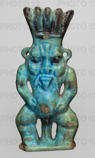 Amulet — god Bes; maker, Bes mythology, Egyptian deity; Late Period, 664–332 BC, Egypt; amulet; height 7.2 cm, width 3.2 cm., A small sculpted figure shown against a plain light gray background, rendered in shades of turquoise, blue, green, and patches of dark brown and tan; the figure has a flared, scalloped headdress that is darker at the top, a stylized face with deep-set eyes and a pronounced triangular beard area, and looped ear ornaments on each side; the torso is compact with arms bent at the elbows resting on the hips, and the lower body shows bent legs separated by two vertical openings, with worn spots and areas of surface discoloration in brown and tan.
