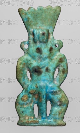 Amulet — god Bes; maker, Bes myth.; Egyptian deity; Late Period, 664–332 BC, Egypt; amulet; height 7.2 cm, width 3.2 cm., A small carved figure in shades of turquoise and aqua with areas of darker blue and green and patches of brown and tan discoloration, showing a humanoid shape with a flared crown-like top, rounded shoulders with holes at each side, a simplified squared head, a torso narrowing at the waist, and stylized legs with open cutouts; surface appears worn and pitted with mottled spots and weathered texture against a plain light gray background.